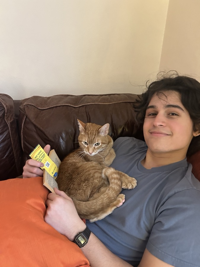 Ian on a couch with a book and an orange cat